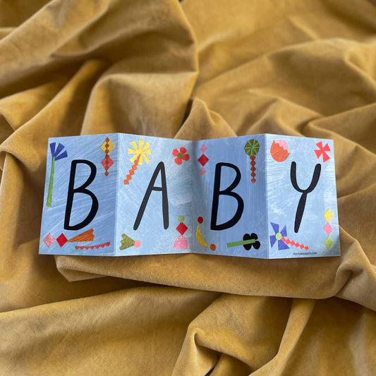 Colorful baby concertina greeting card with 'BABY' on a yellow fabric background by Mortlake Papers by Alice Lickens.