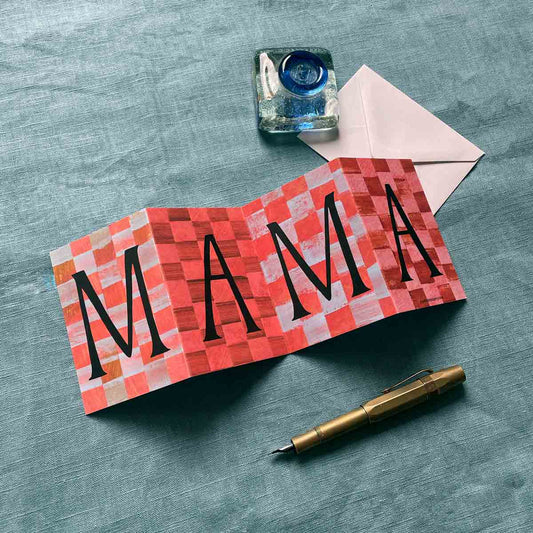 Concertina greeting card by Alice Lickens for Mortlake Papers with 'MAMA' on a checkered pattern, inkwell, envelope, and pen on a textured surface.