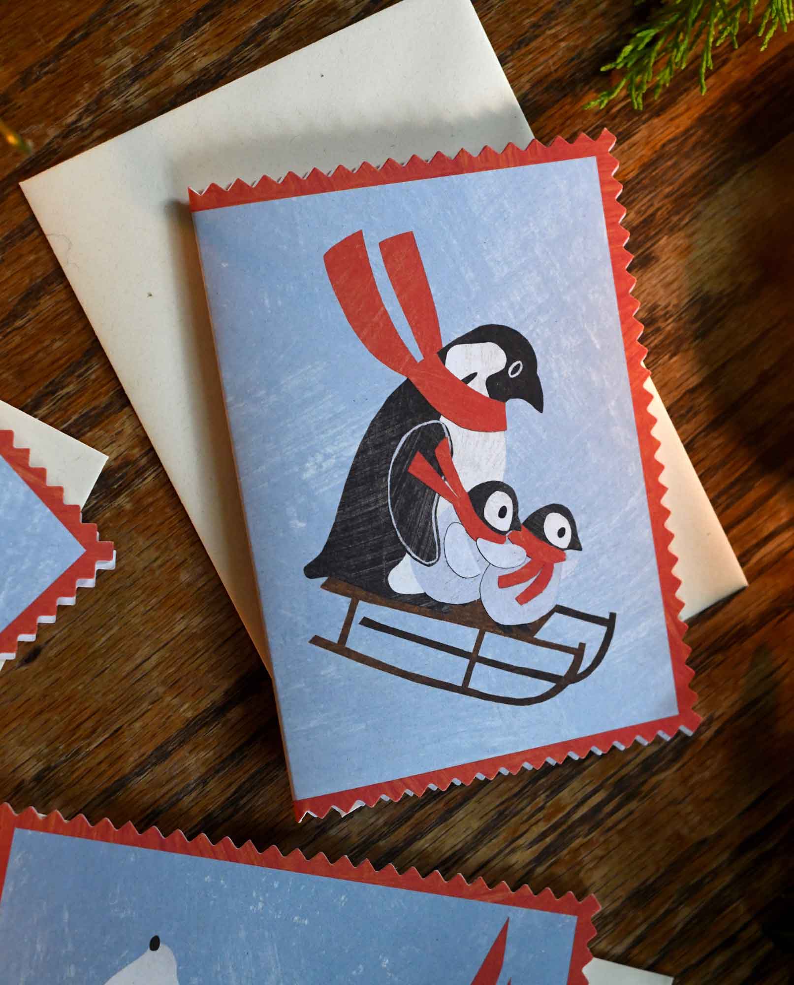 penguin family on a sledge wearing a scarf christmas holiday greeting card by mortlake papers