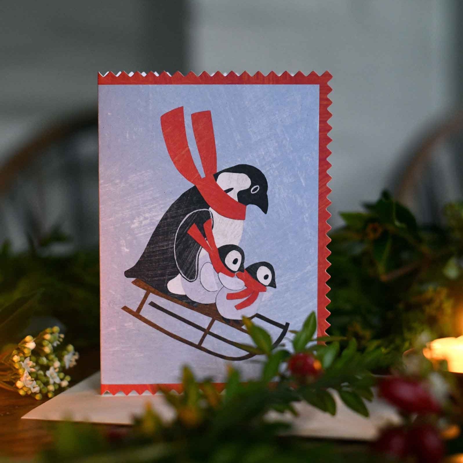 penguin family on a sledge wearing a scarf christmas holiday greeting card by mortlake papers