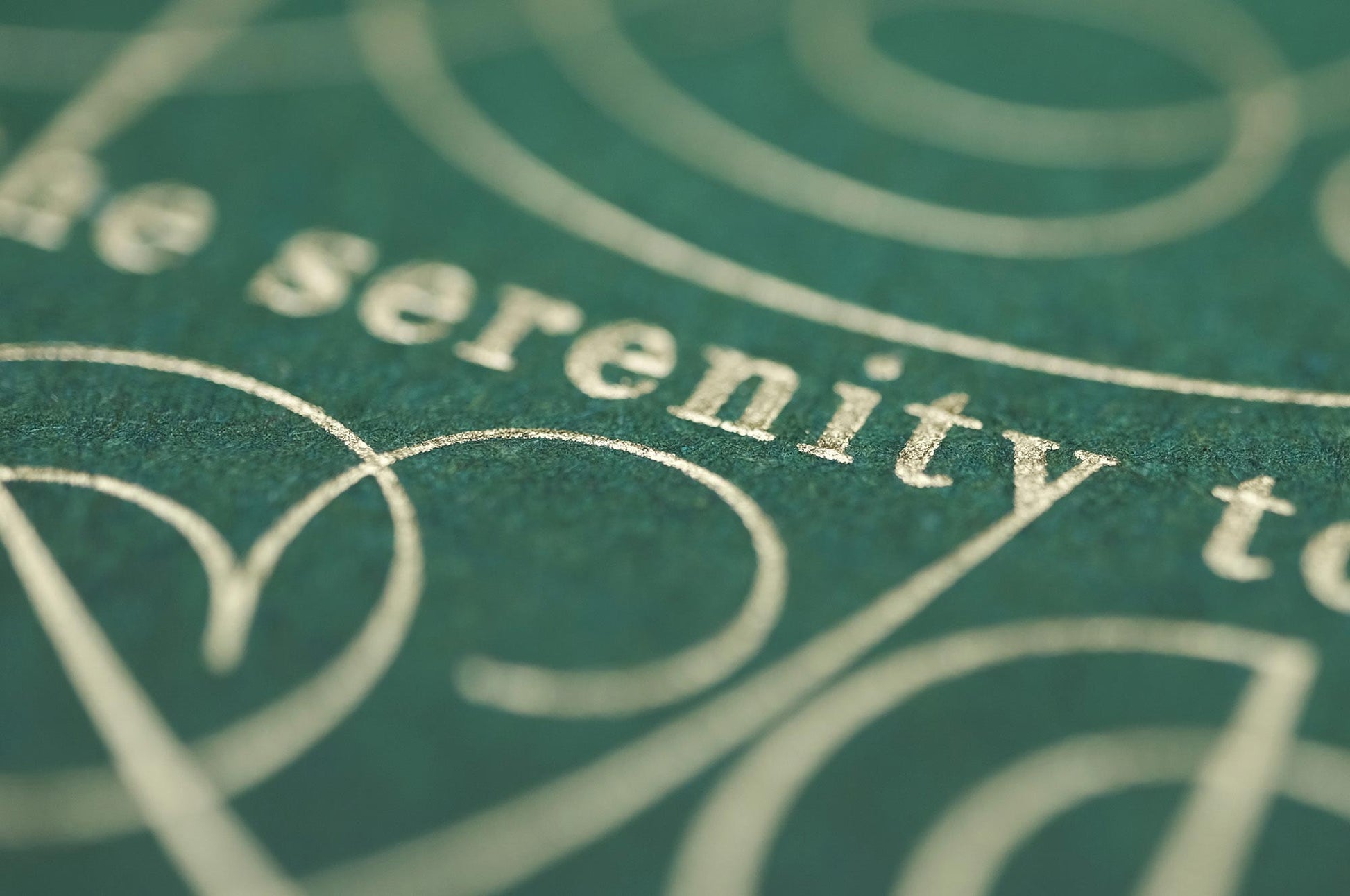The serenity prayer die stamp print by Seb Lester in gold on green. Features text: "god grant me the serenity to accept the things I cannot change, courage to change the things I can and wisdom to know the different. Type in ornate font and flourishes and swirls around the text. Close up detail.
