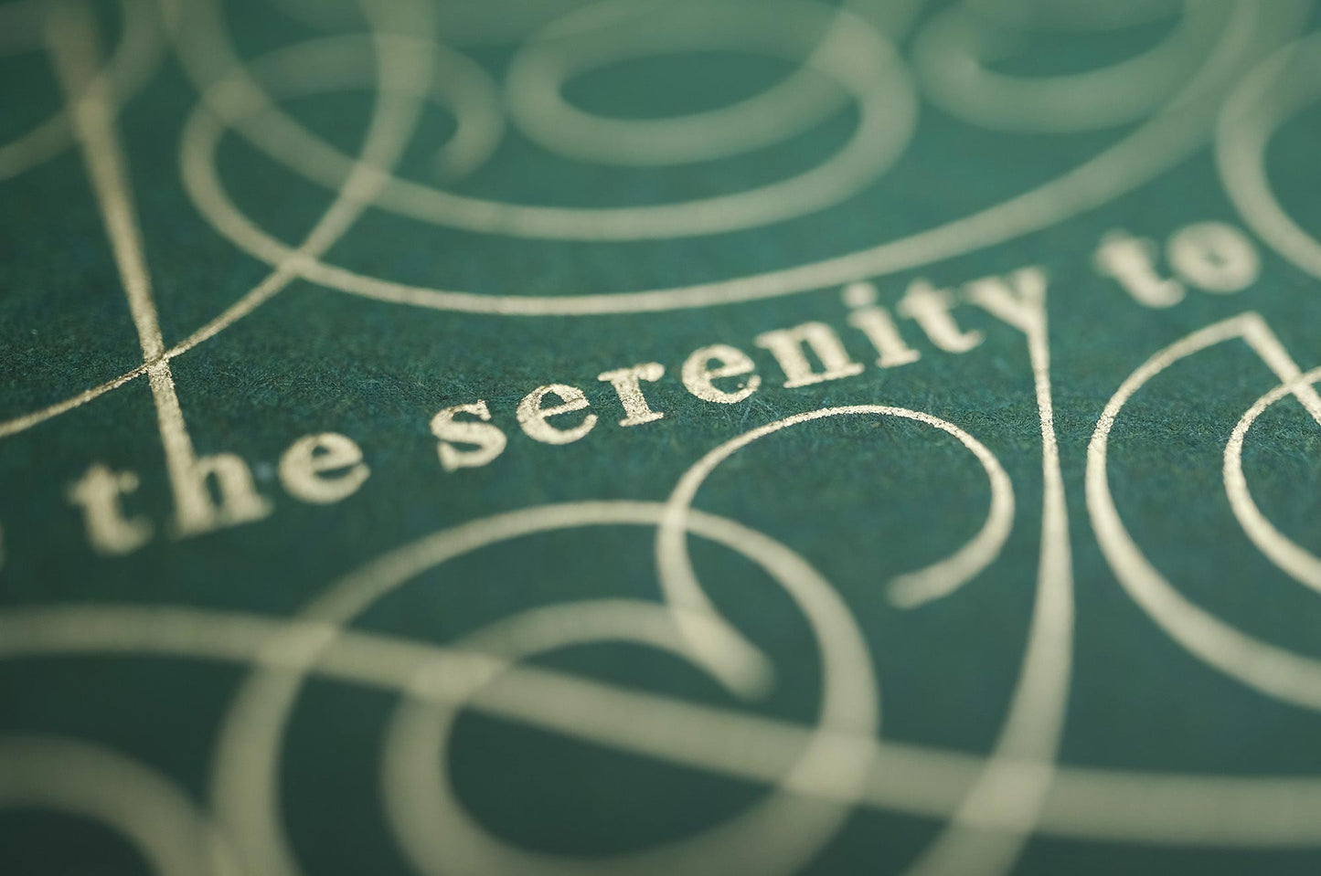 The serenity prayer die stamp print by Seb Lester in gold on green. Features text: "god grant me the serenity to accept the things I cannot change, courage to change the things I can and wisdom to know the different. Type in ornate font and flourishes and swirls around the text. Close up detail.