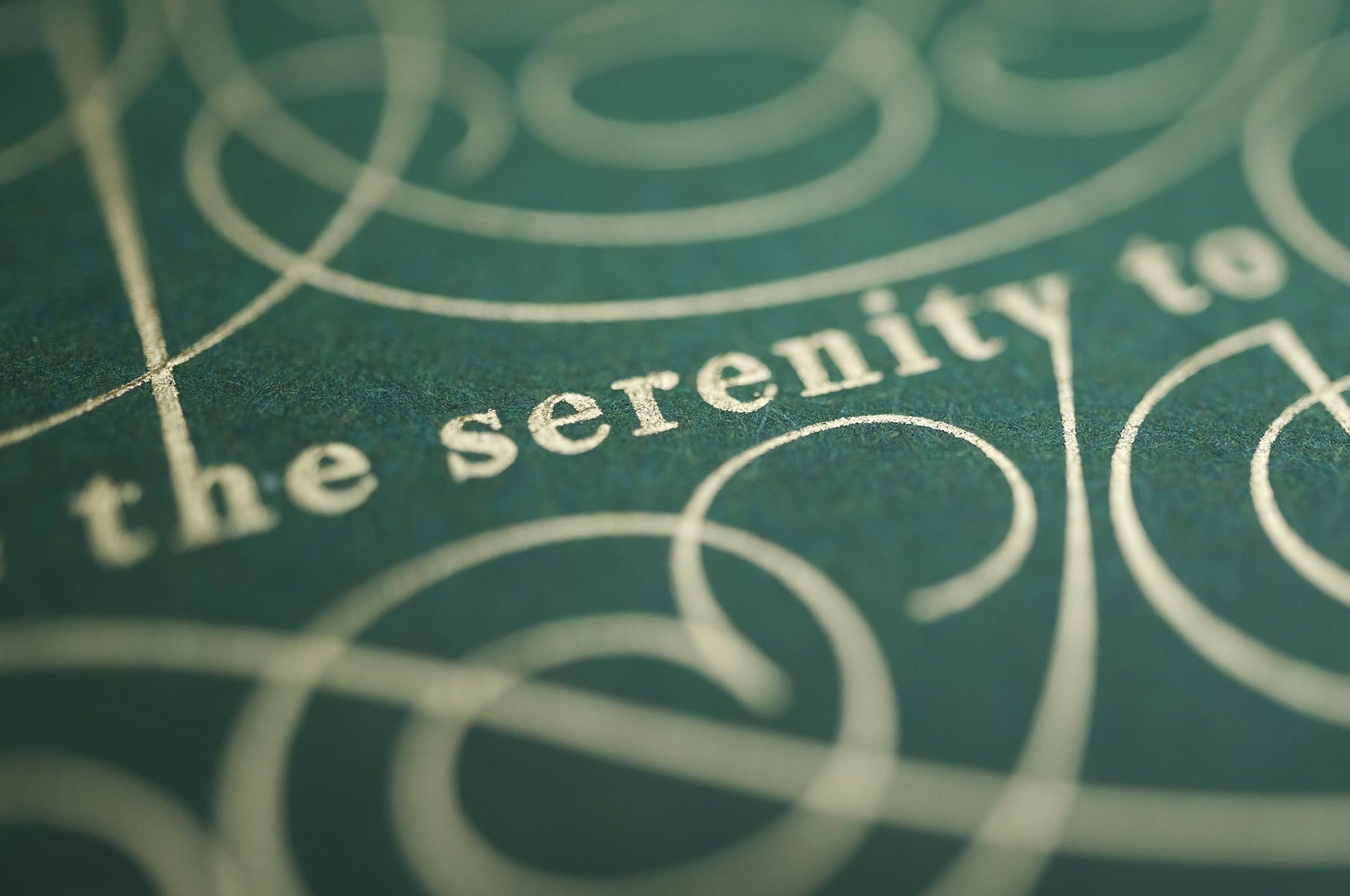 The serenity prayer die stamp print by Seb Lester in gold on green. Features text: "god grant me the serenity to accept the things I cannot change, courage to change the things I can and wisdom to know the different. Type in ornate font and flourishes and swirls around the text. Close up detail.