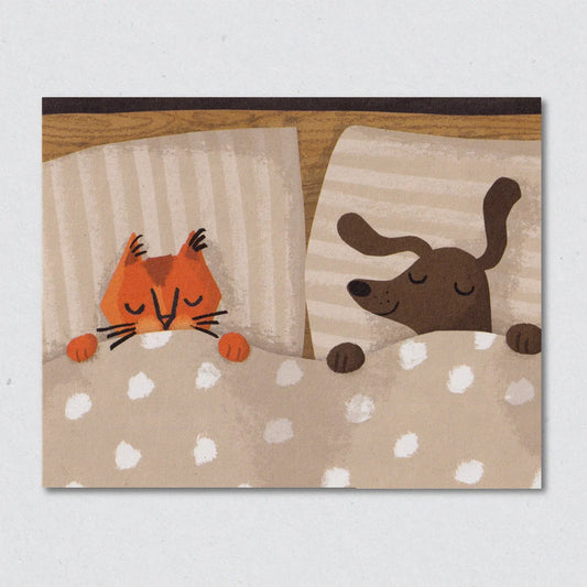 Greeting card with llustration of a cat and a dog lying in bed together on a polka dot blanket by Lisa Jones Studio.