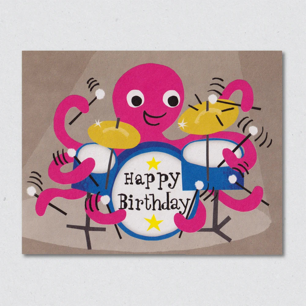 Colorful birthday card with a pink octopus with a blue drumkit with the words 'happy birthday' on a brown background by Lisa Jones Studio.
