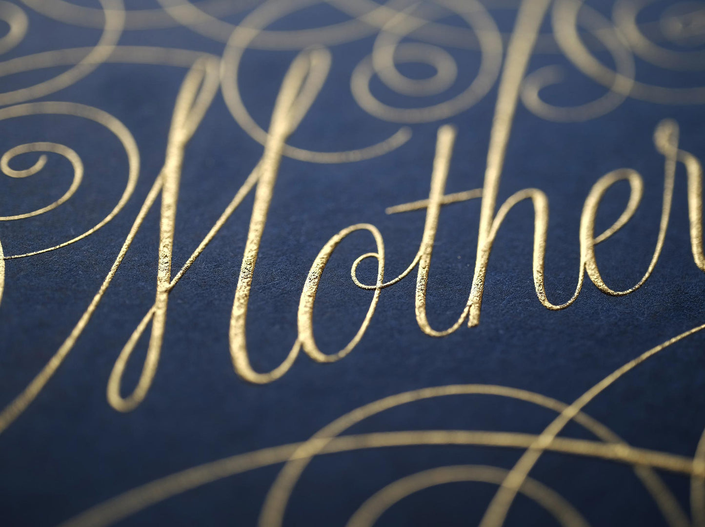 Cursive die stamped artwork by Seb lester. Featuring ornate swirls and swooshes around a swearword. Gold ink on blue paper.