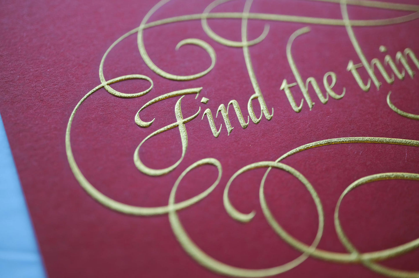 Find the things print by Seb Lester. Die stamp with raised impression. Illustrates the text Find the things you love with flourishes and swirls in gold on red. Close up detail.