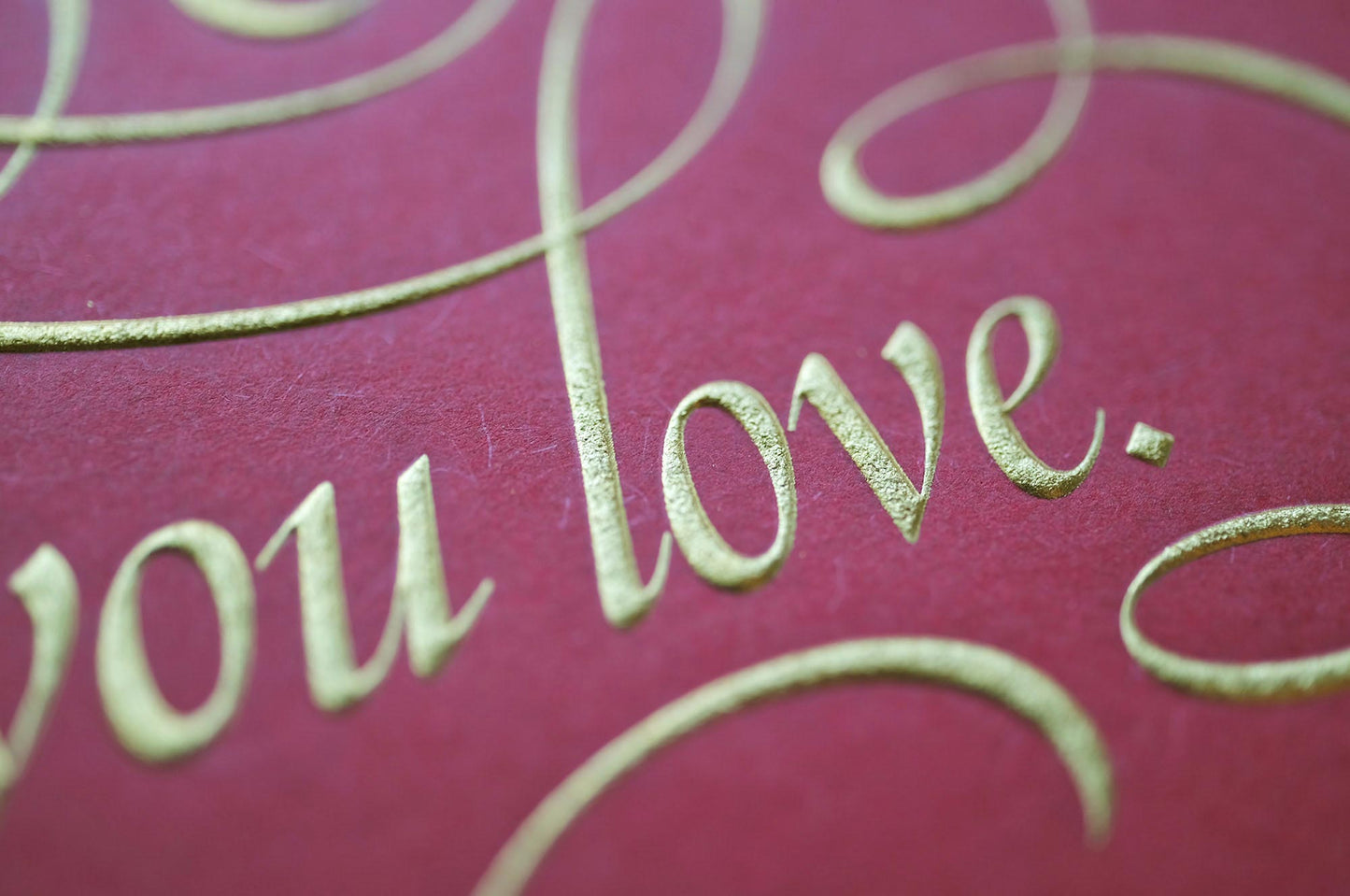 Find the things print by Seb Lester. Die stamp with raised impression. Illustrates the text Find the things you love with flourishes and swirls in gold on red. Close up detail.