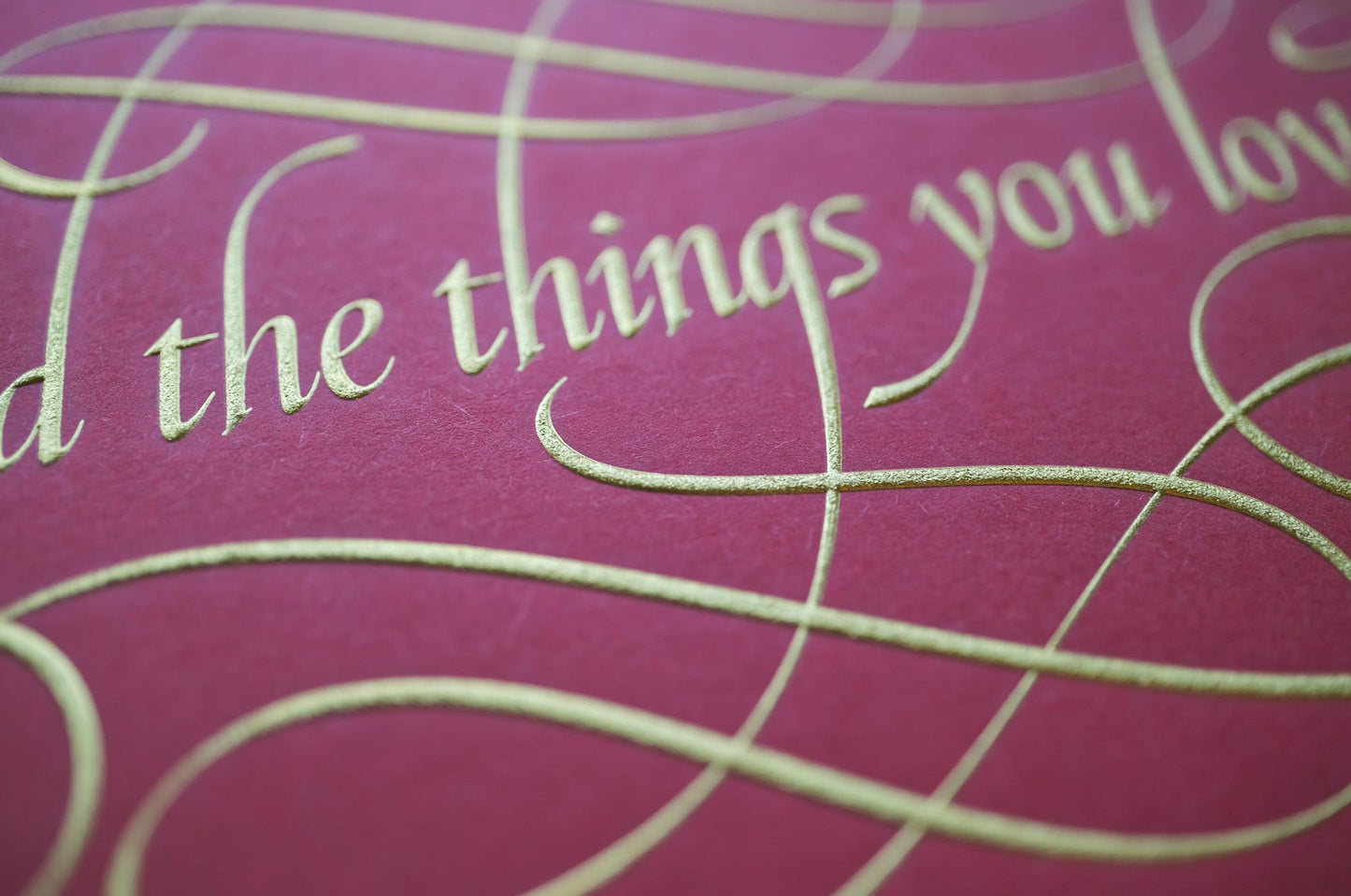 Find the things print by Seb Lester. Die stamp with raised impression. Illustrates the text Find the things you love with flourishes and swirls in gold on red. Close up detail.