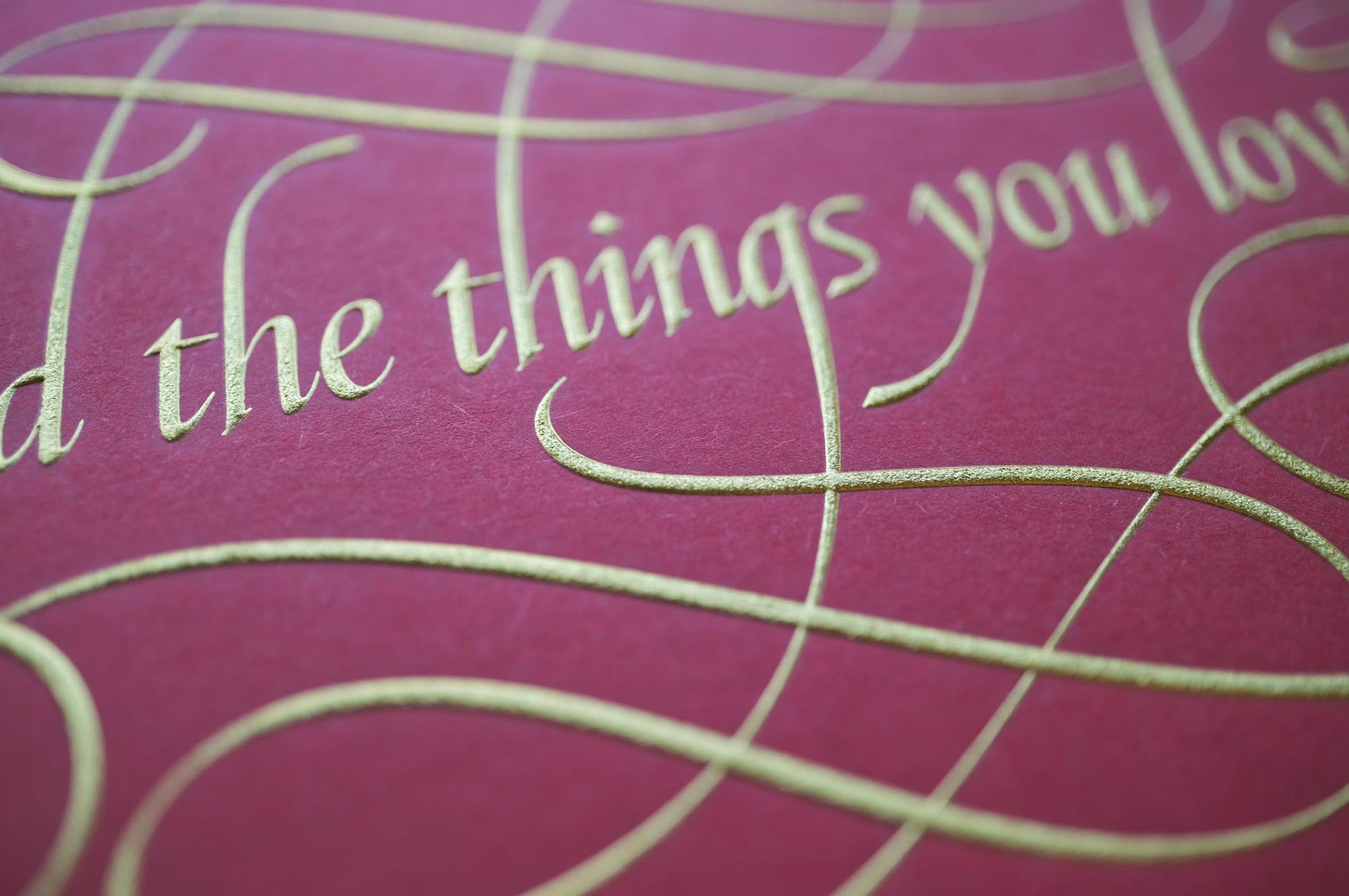Find the things print by Seb Lester. Die stamp with raised impression. Illustrates the text Find the things you love with flourishes and swirls in gold on red. Close up detail.