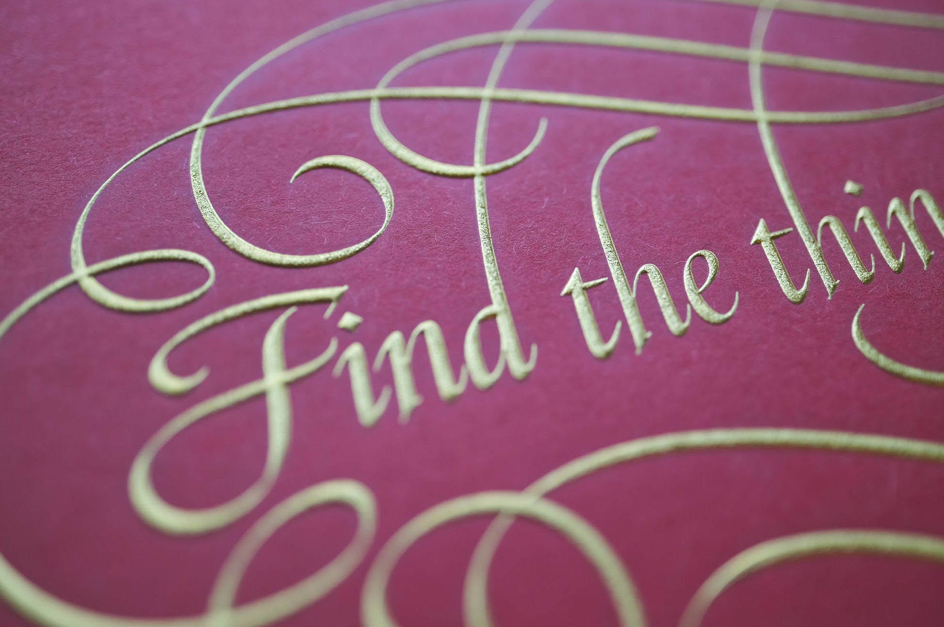 Find the things print by Seb Lester. Die stamp with raised impression. Illustrates the text Find the things you love with flourishes and swirls in gold on red. Close up detail.