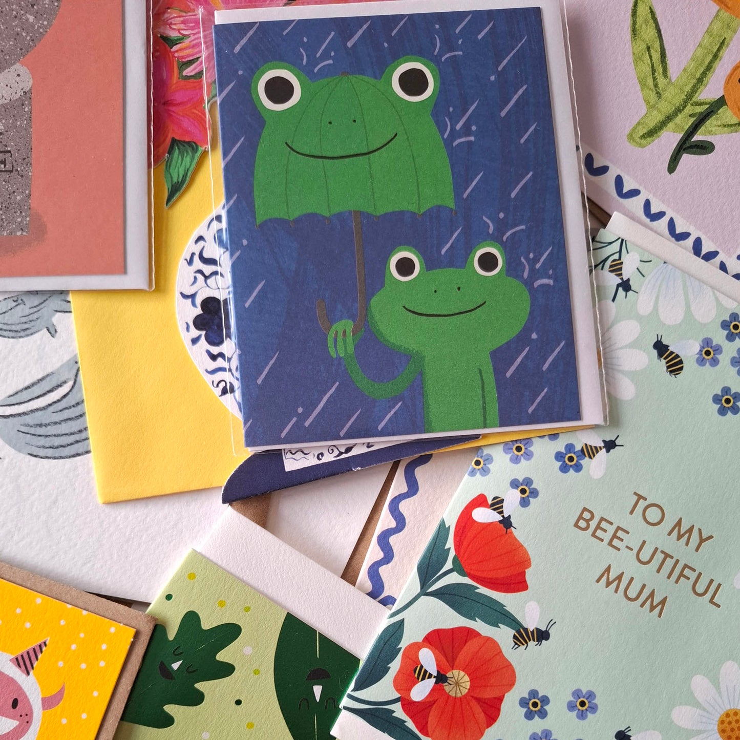Collection of greeting cards with various designs, including frogs and floral patterns.