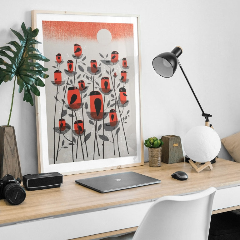 Modern home office desk with a laptop, lamp, and framed 'Siskin Tree' original screen print by contemporary printmaker and artist, Graham Carter, on a white wall.