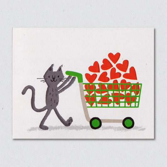 Unexpected Items greeting card by Lisa Jones Studio with an illustration of a cat pushing a green shopping cart filled with red hearts on a white background.