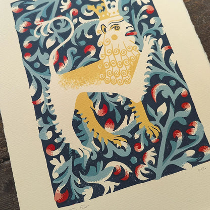 Detail of decorative screen print of a lion with a crown on a blue floral background by contrmporary printmaker and artist, Tom Frost, placed on a wooden surface.
