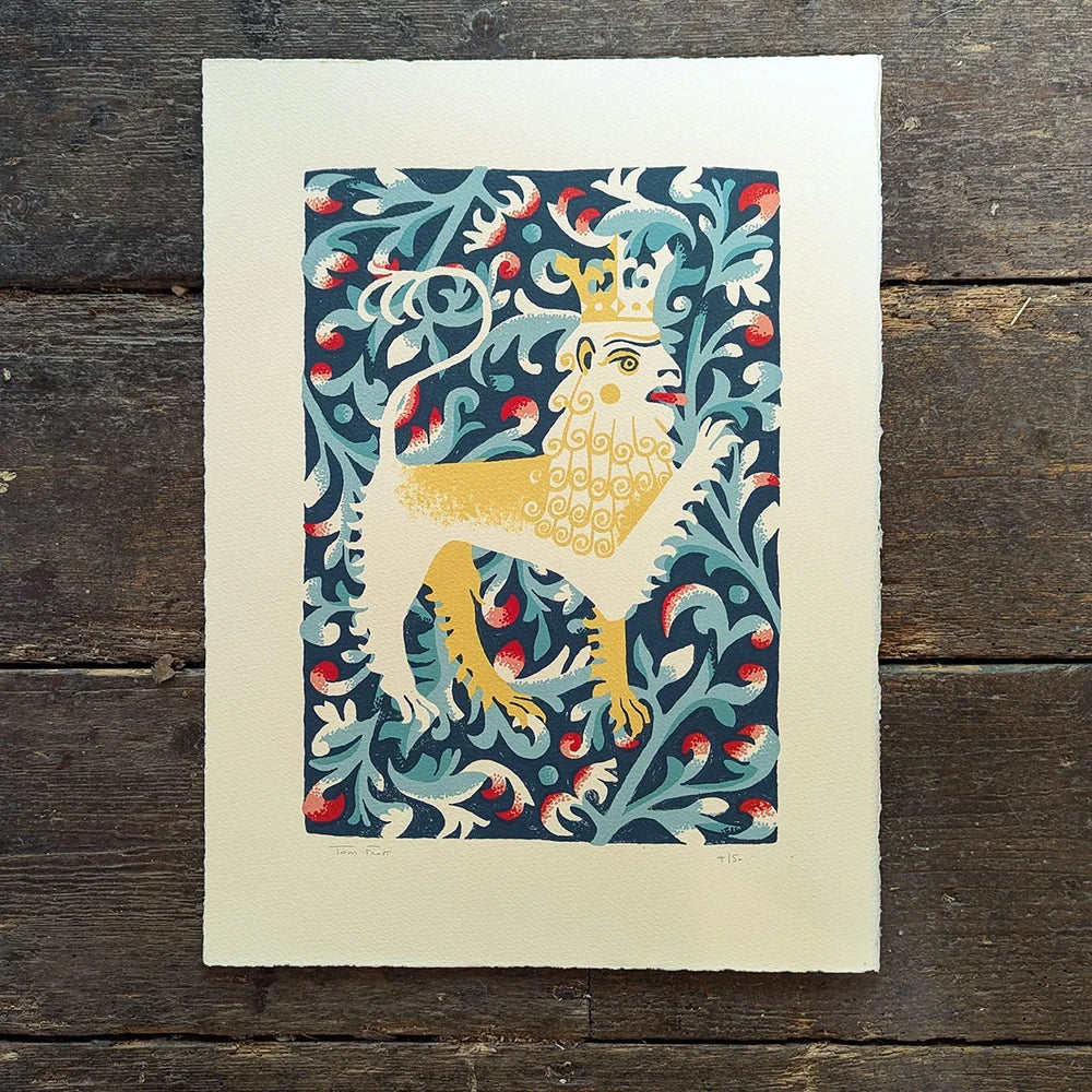 Decorative screen print of a lion with a crown on a blue floral background by contrmporary printmaker and artist, Tom Frost, placed on a wooden surface.