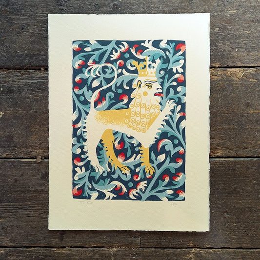 Decorative screen print of a lion with a crown on a blue floral background by contrmporary printmaker and artist, Tom Frost, placed on a wooden surface.