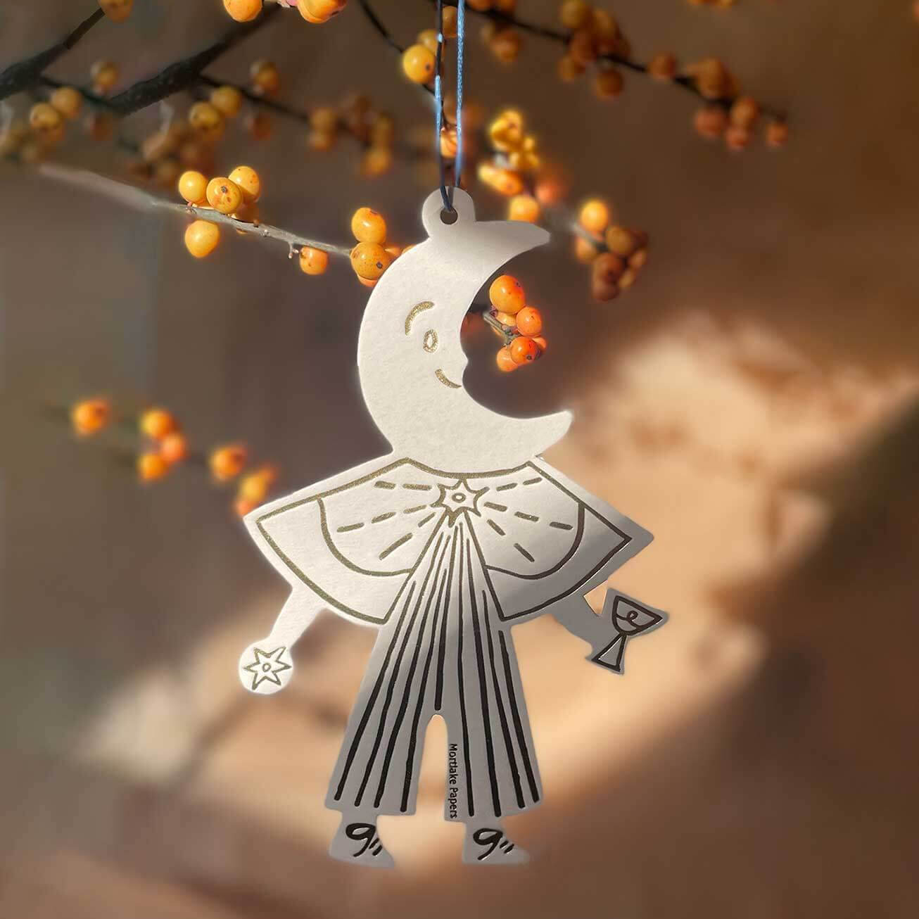Decorative ornament shaped like a stylized figure with a crescent moon on a branch with orange berries.