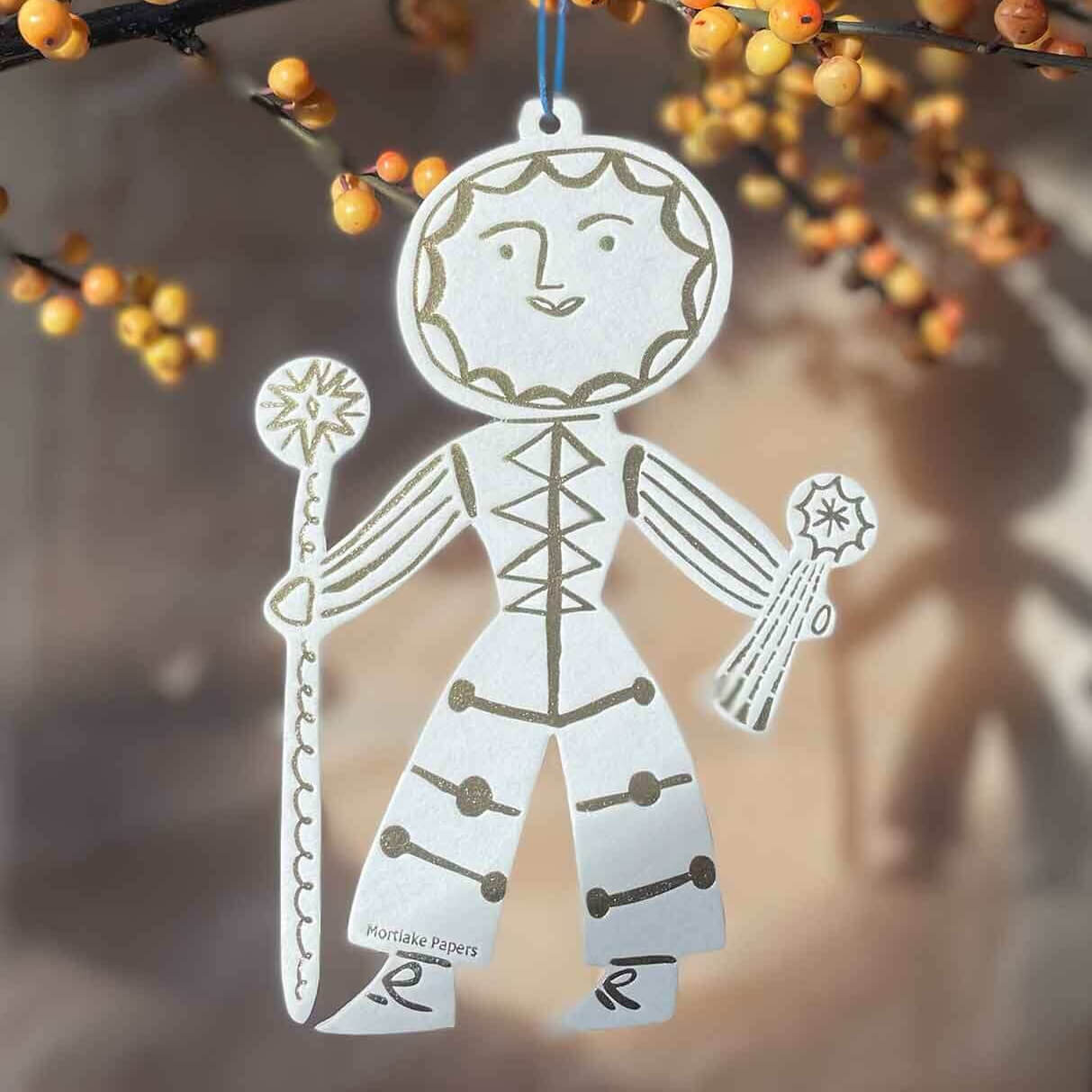 Decorative paper cutout of a sun man figure with autumn berries in the background