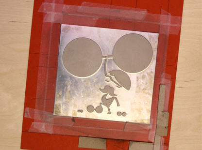 Letterpress printing metal plate with circular cutouts and a silhouette of a strong man, framed by red paper.